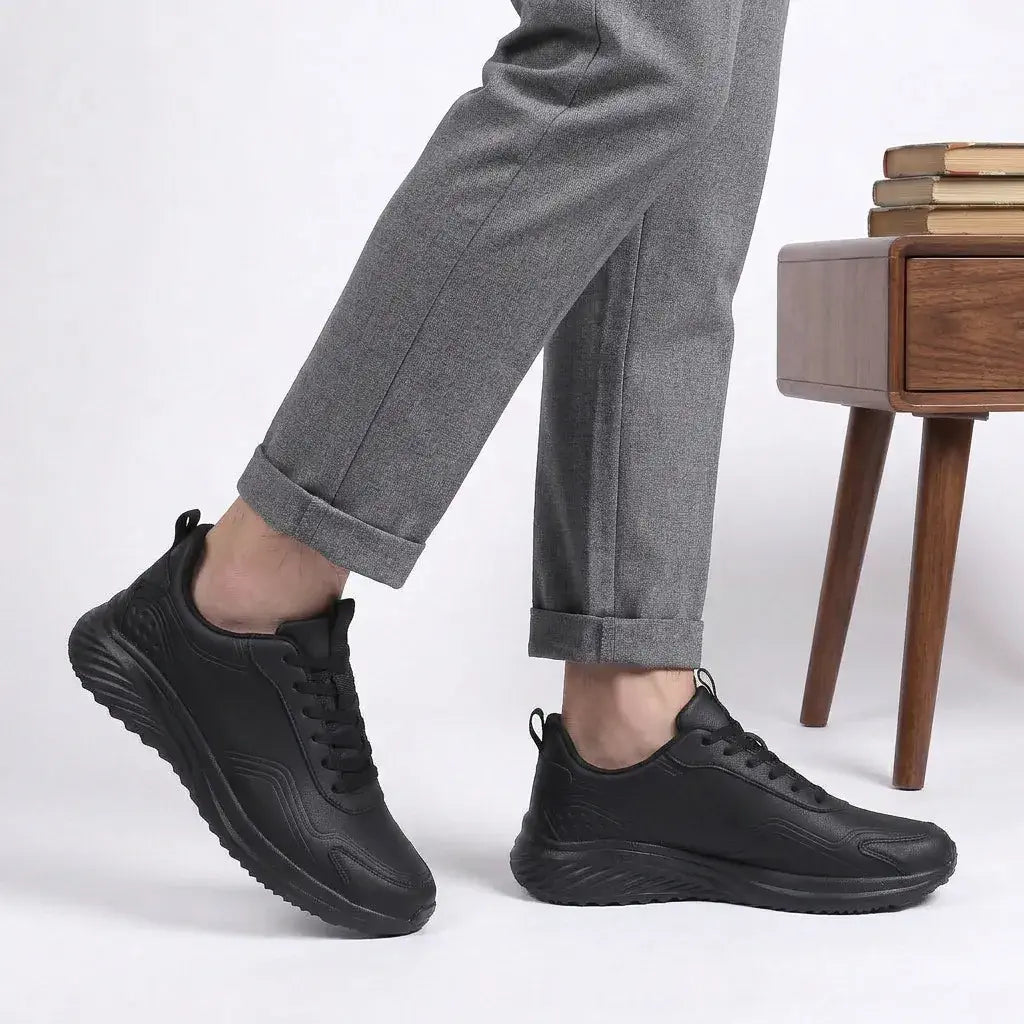 HexoComfy™ Men's Orthopedic Performance Sneakers in Black worn with gray trousers beside a wooden side table